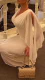 Seated view of the ivory floor-length gown showing the gathered bust and draped sleeve panels
