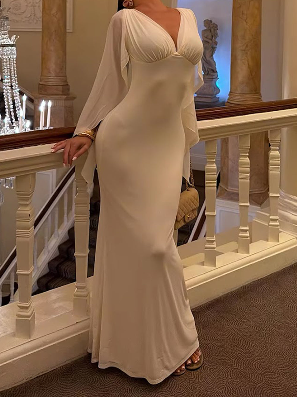 Seated model wearing the black gown with dramatic draped cape sleeves and V neckline
